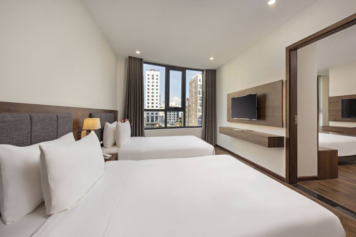 Una habitación de hotel con dos camas, televisión, escritorio y ventana con vista a la ciudad.