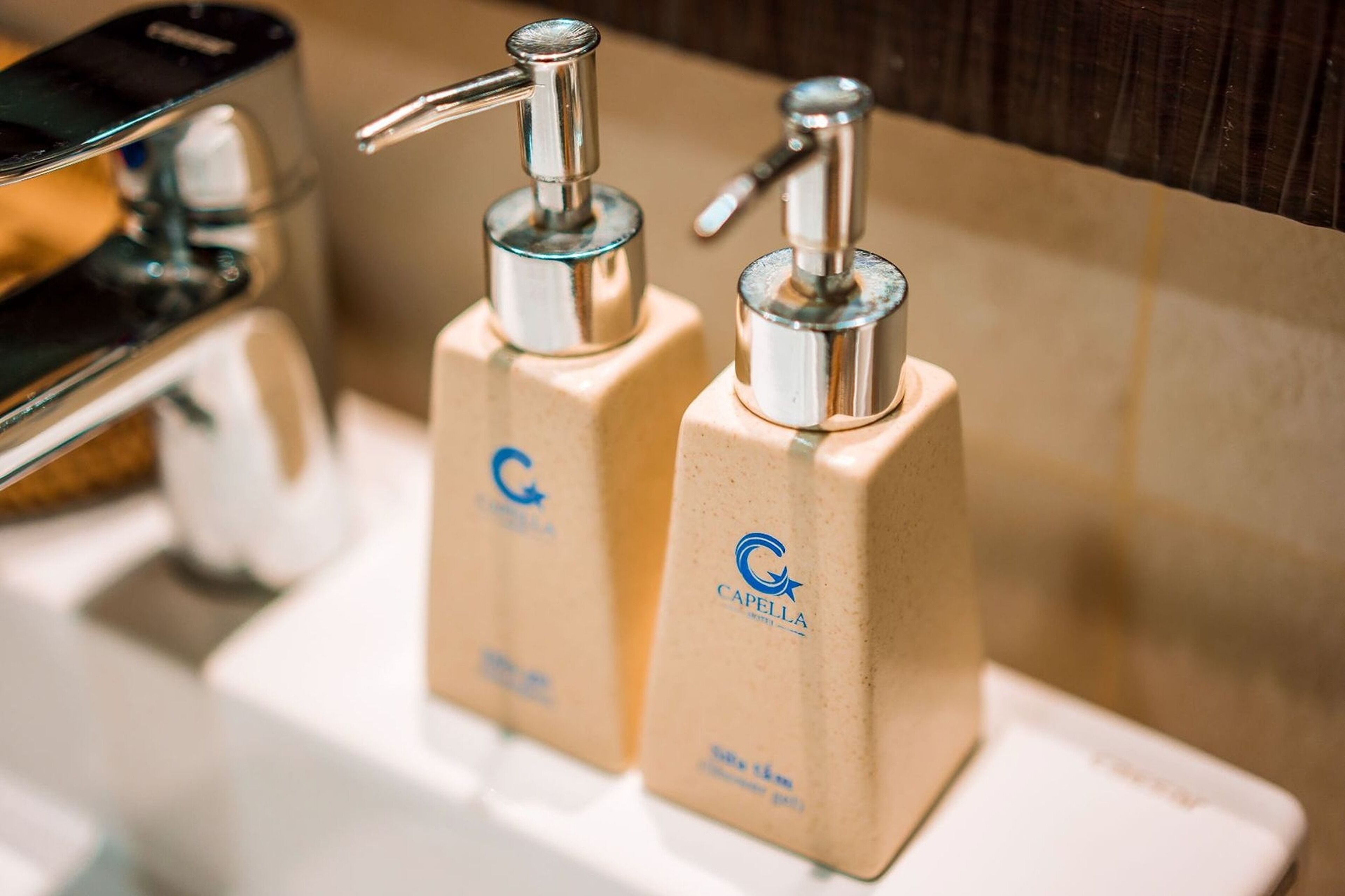 Dos dispensadores de jabón de manos con bomba metálica y base color beige, ubicados sobre un lavabo blanco.