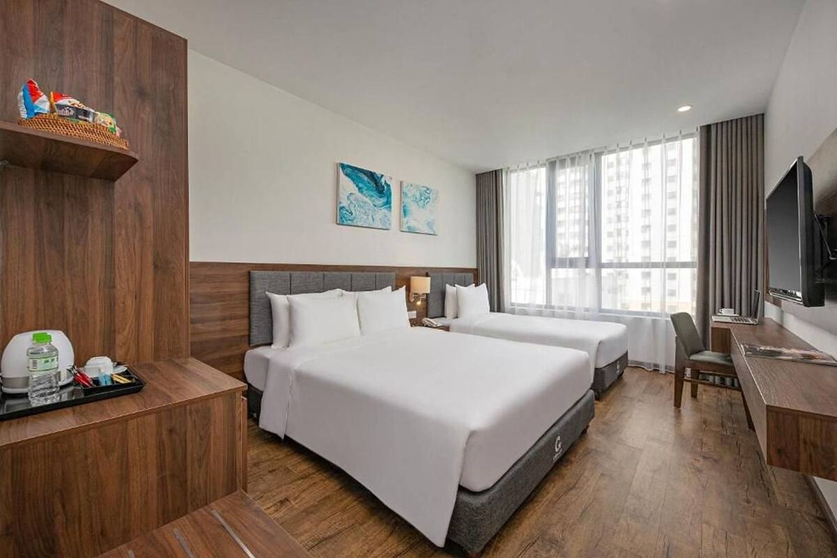 Habitación de hotel con dos camas, un escritorio, un televisor y una ventana con cortinas.
