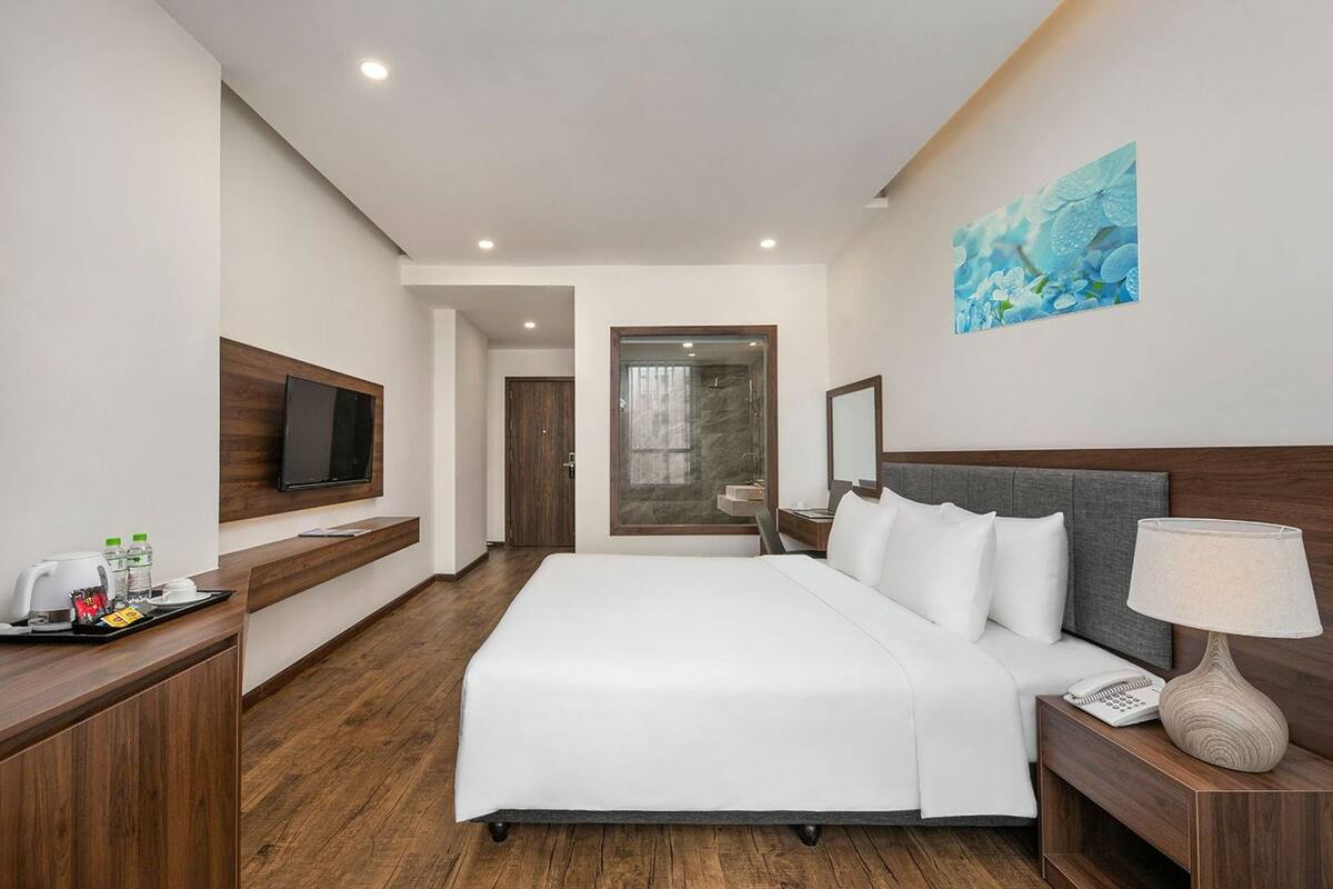 Una habitación de hotel moderna con una cama grande, un televisor de pantalla plana, un escritorio de madera con cafetera y un cuadro en la pared.