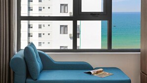 Una habitación con un sofá azul y una ventana con vistas a un edificio y al mar.