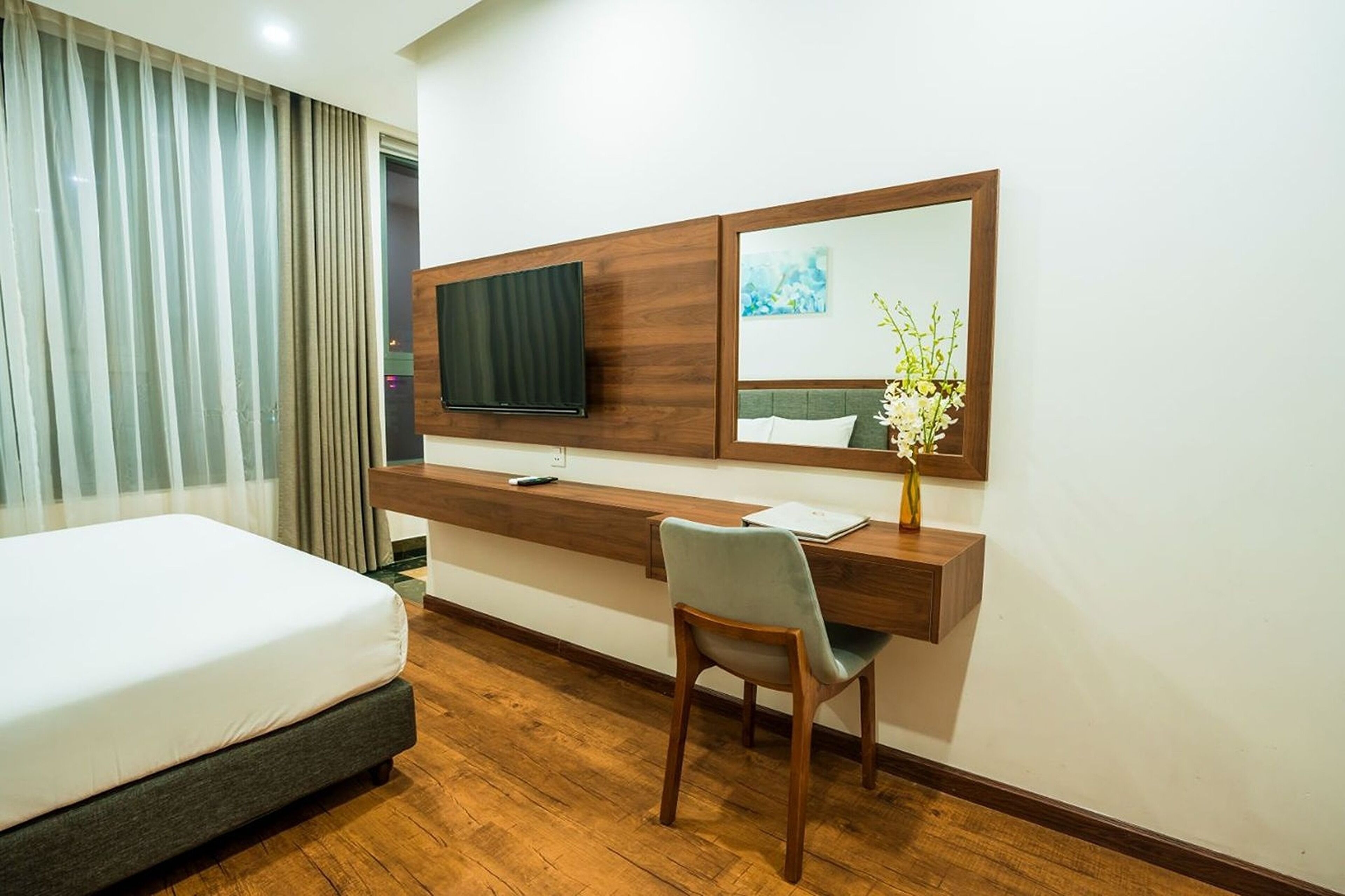 Una habitación de hotel con una cama, un escritorio con una silla, un televisor y un espejo.