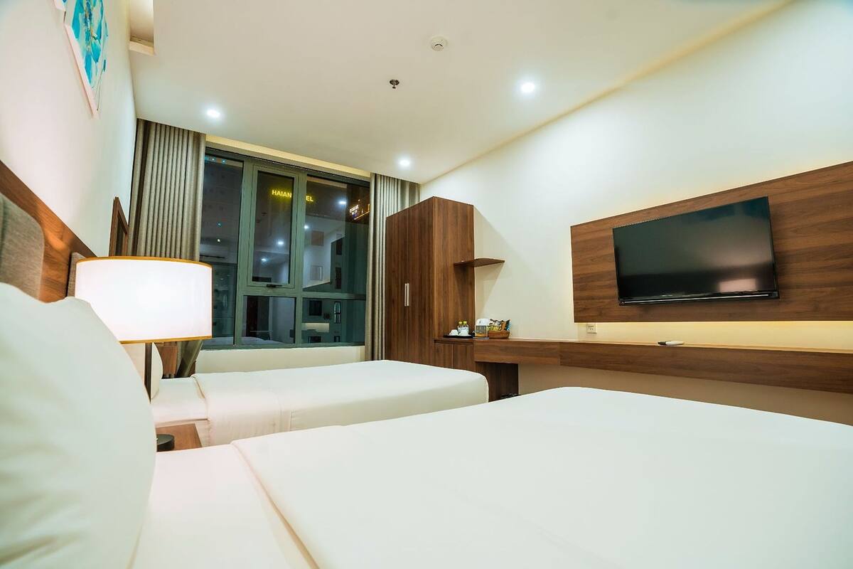 Habitación de hotel con dos camas, televisión montada en la pared, escritorio y ventana con cortinas.
