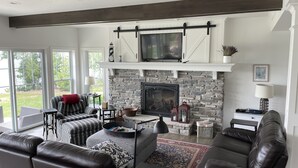 A modern living room with a stone fireplace, leather sofas, and a large TV mounted above the fireplace.