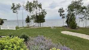 A landscaped garden with a view of the sea, featuring a grassy area, a white fence, and various shrubs.