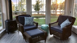 A room with two wicker chairs, a small round table, and a wood-burning stove.