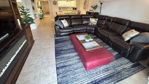 A living room with a sectional sofa, a red ottoman, a coffee table, and a television on a wooden cabinet.