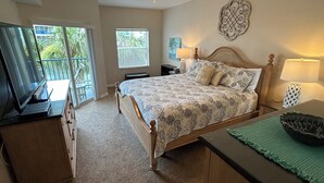A bedroom with a bed, a desk, a laptop, a ceiling fan, and a view of the outdoors.