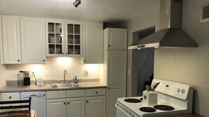 Une cuisine avec des meubles blancs, un lave-vaisselle encastré, une cuisinière et un évier.