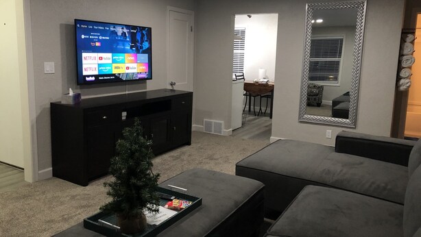 Un salon avec un téléviseur à écran plat fixé au mur, un petit sapin de Noël posé sur une table basse et un grand miroir sur le mur.
