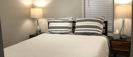 A neatly made bed with striped pillows, a ceiling fan, and two bedside lamps.