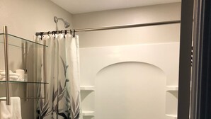 Une salle de bain comprenant des toilettes, une étagère en verre avec des serviettes, un rideau de douche et une baignoire.
