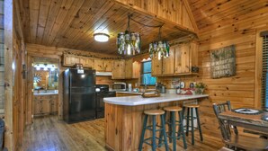 A wooden cabin kitchen with a central island, bar stools, and a dining table. - Serendipity - Cherry Log (Cherry Log)