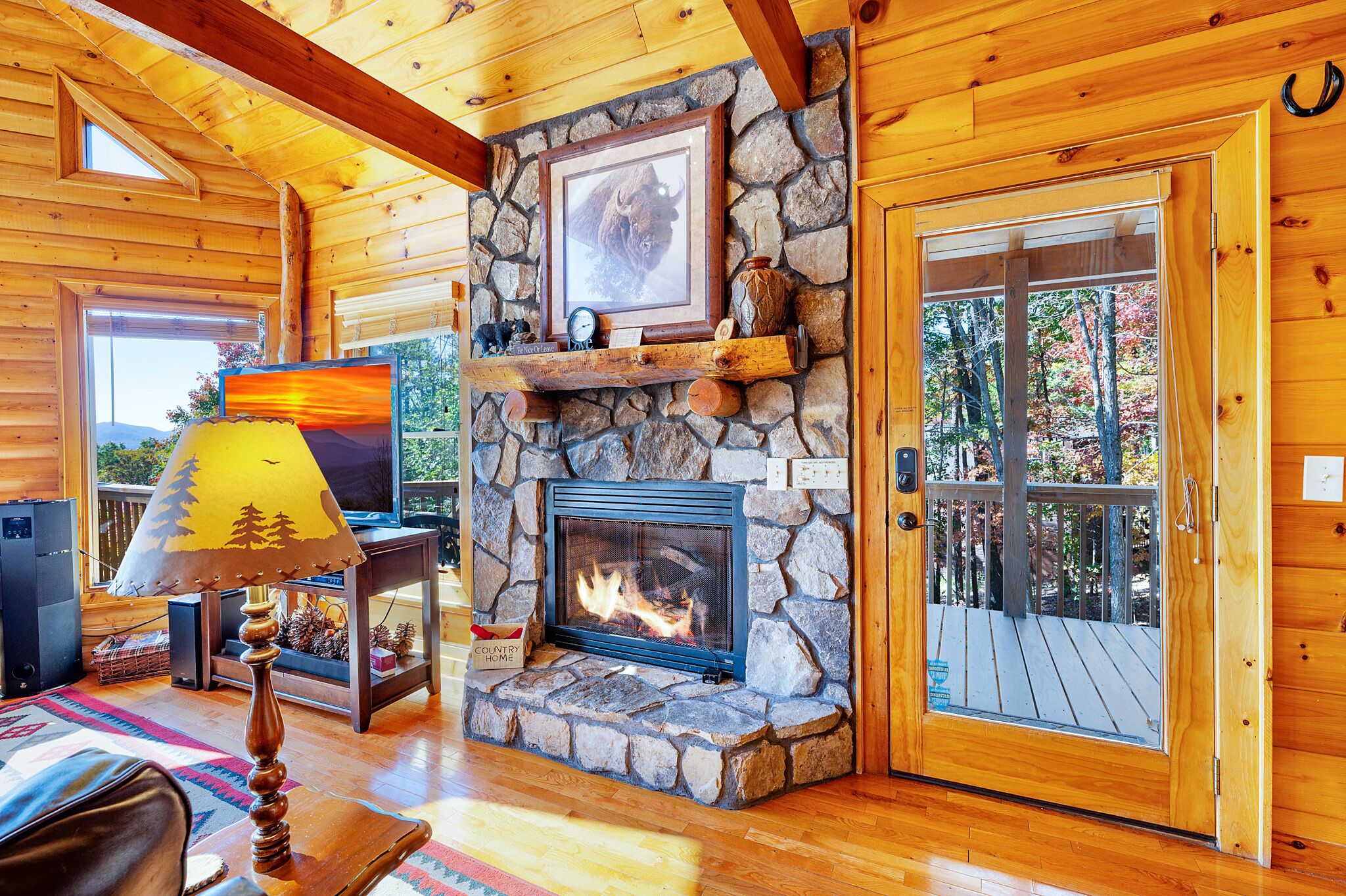 Un intérieur de chalet chaleureux avec une cheminée en pierre, des murs en bois, un téléviseur et une grande fenêtre.