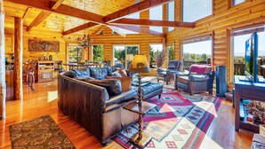 Un intérieur spacieux de chalet en bois, avec un grand canapé en cuir, un coin repas et une vue sur l’extérieur.
