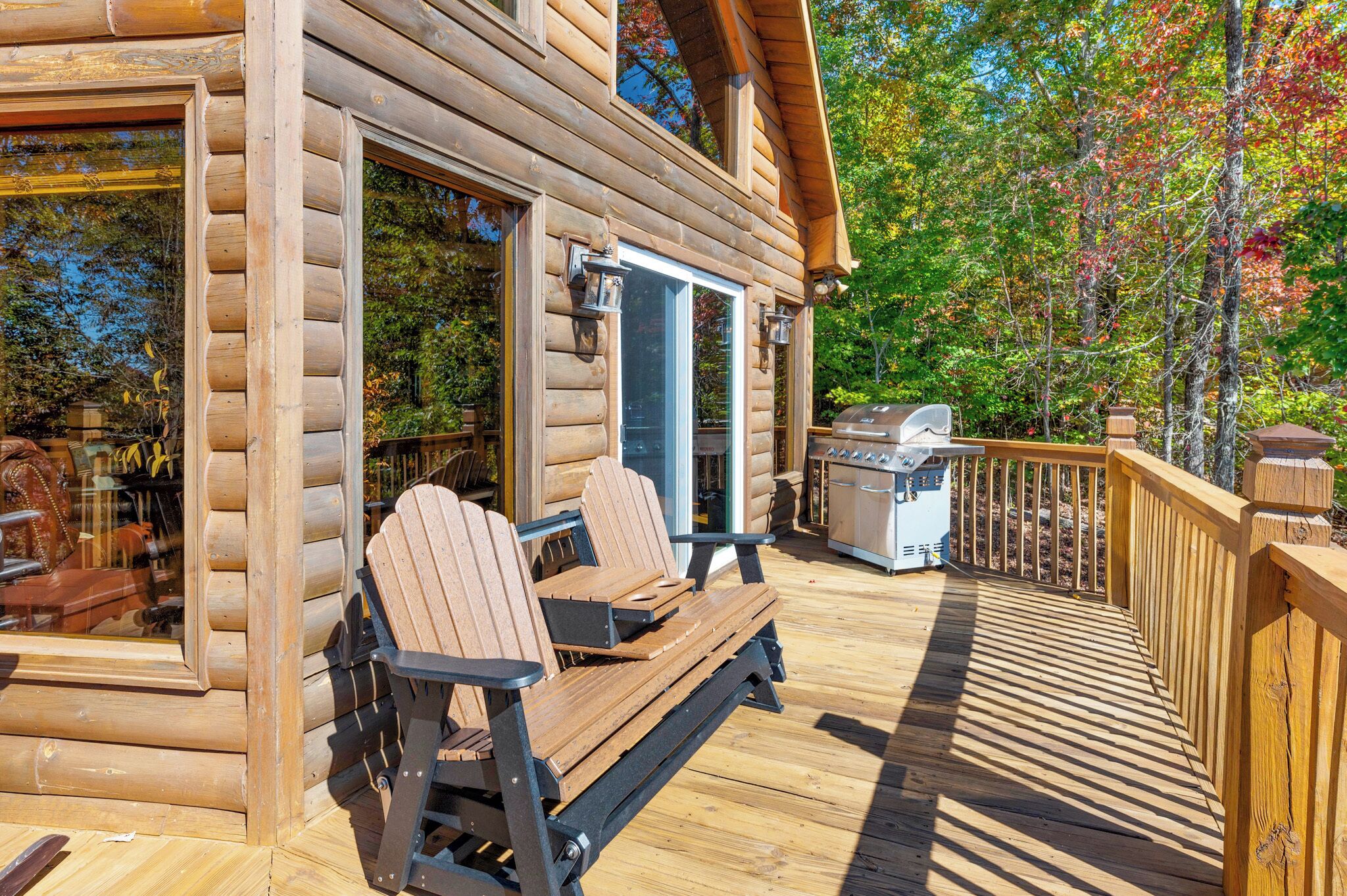 Une cabane en bois dotée d’une terrasse, de deux fauteuils Adirondack et d’un barbecue.