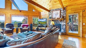 Un intérieur de chalet en bois spacieux, avec un grand canapé en cuir, un téléviseur et une cheminée en pierre.