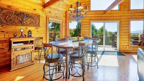 L’intérieur d’un chalet en bois comprend un coin repas, un lustre et de grandes fenêtres.