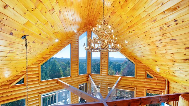 Une cabane en bois avec un plafond haut et un lustre. De grandes fenêtres offrent une vue sur un paysage boisé.