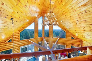 Eine Holzhütte mit hohen Decken und einem Kronleuchter. Große Fenster bieten Blick auf eine bewaldete Landschaft.
