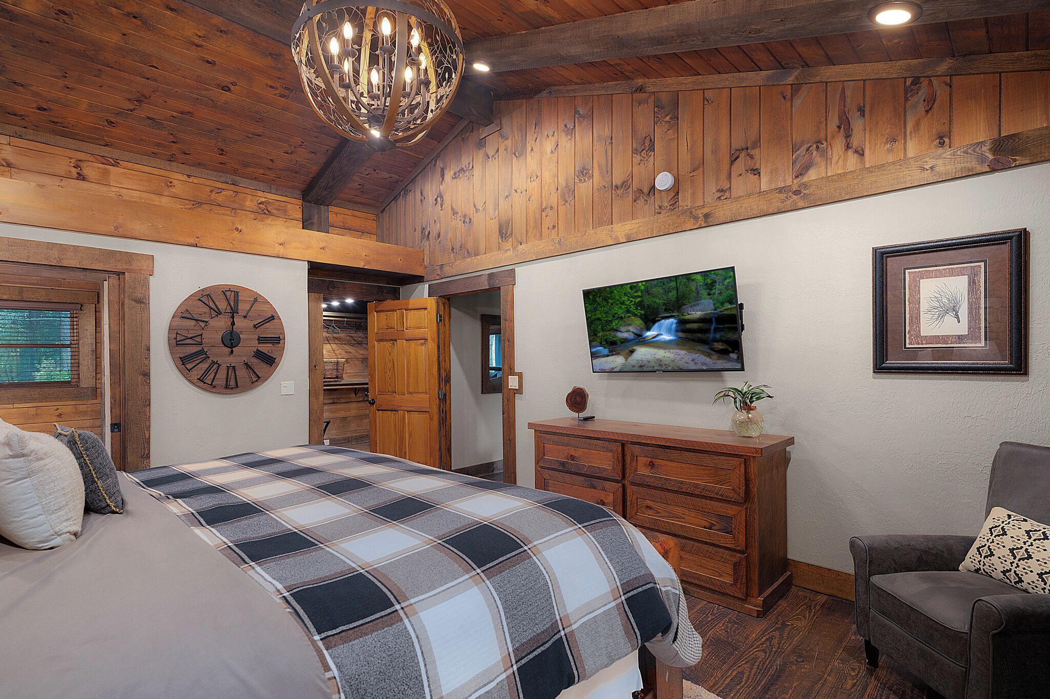 Un dormitorio con una cama grande, techo de madera, un reloj, un televisor y un aparador.