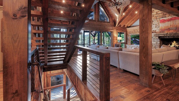 Un vaste espace de vie agrémenté d’un escalier en bois, d’une cheminée en pierre et d’une grande fenêtre donnant sur un paysage verdoyant.
