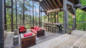 Une terrasse en bois avec un canapé rouge, une table et des chaises, le tout entouré de grands arbres.