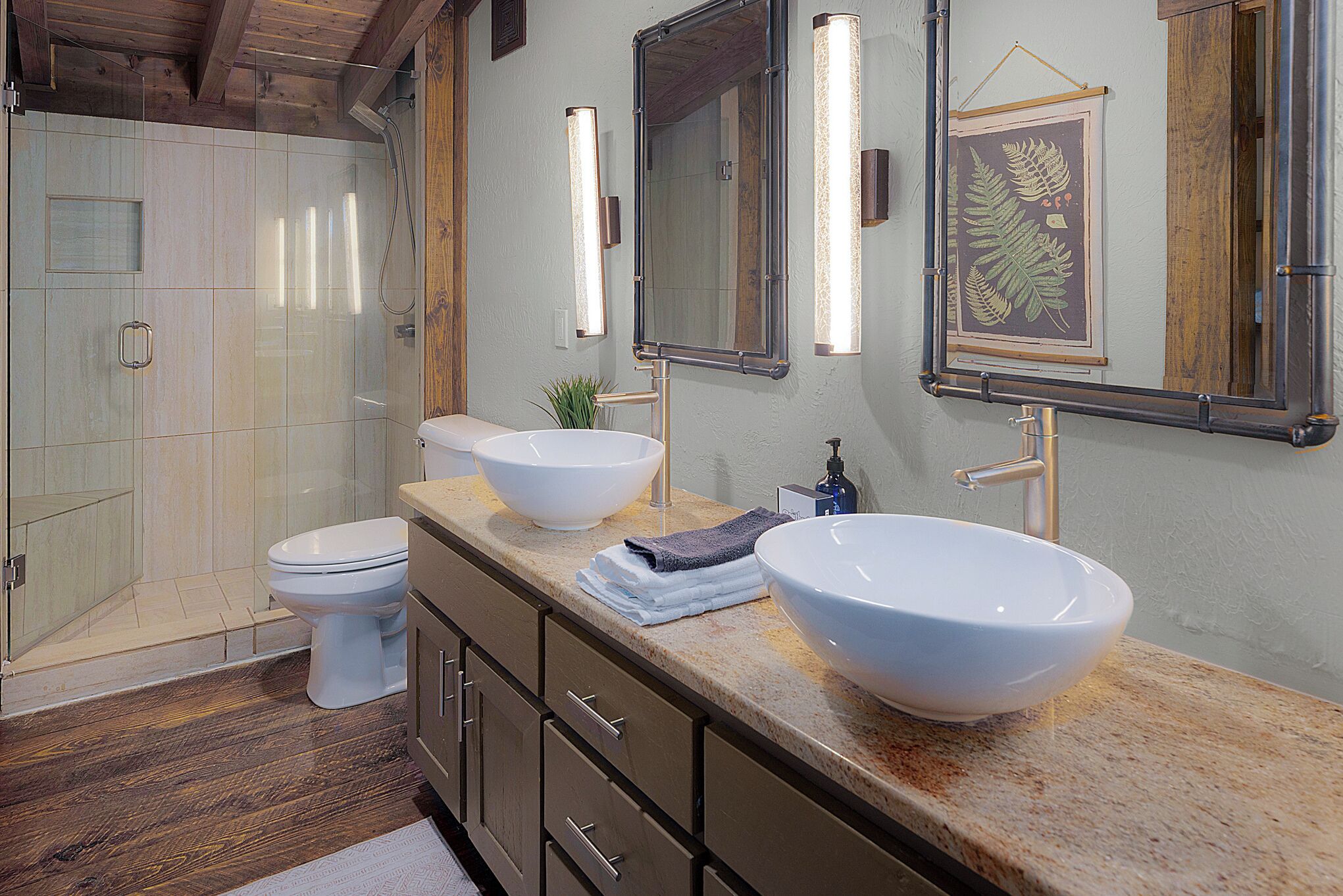 A modern bathroom with a glass shower enclosure, a white toilet, and a vanity with two large sinks and a mirror.
