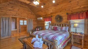 A log cabin bedroom with a large bed, wooden furniture, a ceiling fan, and a window with blinds.