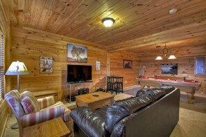 Ein gemütliches Holzhaus-Interieur mit einer Couch, einem Billardtisch, einem Fernseher und einem Kamin.