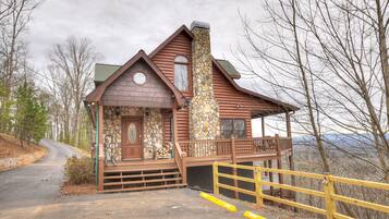 A log cabin with a stone chimney, a porch, and a view of the surrounding landscape.