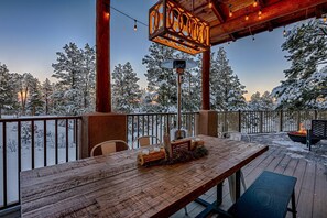 Een houten terras met een tafel en stoelen, omgeven door met sneeuw bedekte bomen, en een bordje met de tekst 'COOK'.