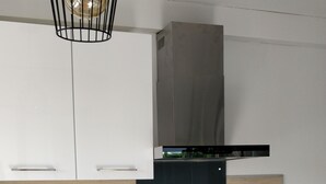 Uma cozinha moderna com armários brancos, bancada de madeira, pia de aço inoxidável, coifa preta e forno embutido.