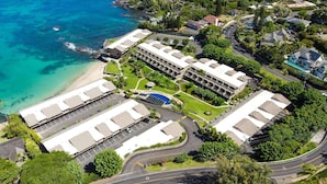 Vista aérea de un hotel frente al mar con varias construcciones, estacionamiento y piscina.