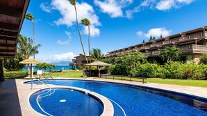 Una piscina con un jacuzzi circular, rodeada de palmeras y un edificio con balcones.