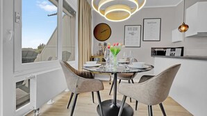 A modern dining area with a round table, four chairs, a vase with flowers, a clock, and framed guides on the wall. - Seaside SA 140 - Seaside, 2 Zi, 65m², Balkon, Meerblick, 2. OG Fahrstuhl (Scharbeutz)