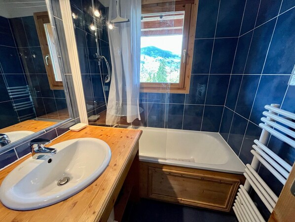 A bathroom with a wooden vanity, a white sink, a bathtub, and a window with a view of greenery. - Ski-in/ski-out apartment, 2 bedrooms, terrace and covered parking - La Clusaz (La Clusaz)