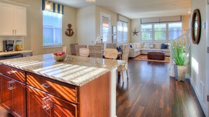 A spacious kitchen with a large island, wooden cabinets, and a dining area with wicker chairs. - Our Beach Adventure - Oyhut Bay Seaside Village (Ocean Shores)