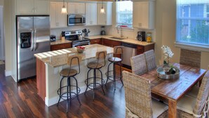 A kitchen with a central island, bar stools, a dining table with wicker chairs, and a sign that reads "BEACH HOUSE". - Our Beach Adventure - Oyhut Bay Seaside Village (Ocean Shores)
