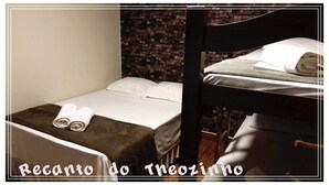Un lit simple avec une tête de lit marron, du linge de lit blanc et deux serviettes enroulées au pied du lit. Le mur derrière le lit est décoré d’un motif en briques.