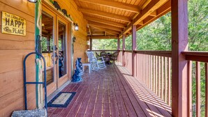 Una cabaña de madera con un porche cubierto, un letrero que dice "The Cabin is My Happy Place" y mobiliario de exterior.