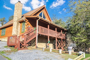 A log cabin with a stone chimney, wooden deck, and a porch.