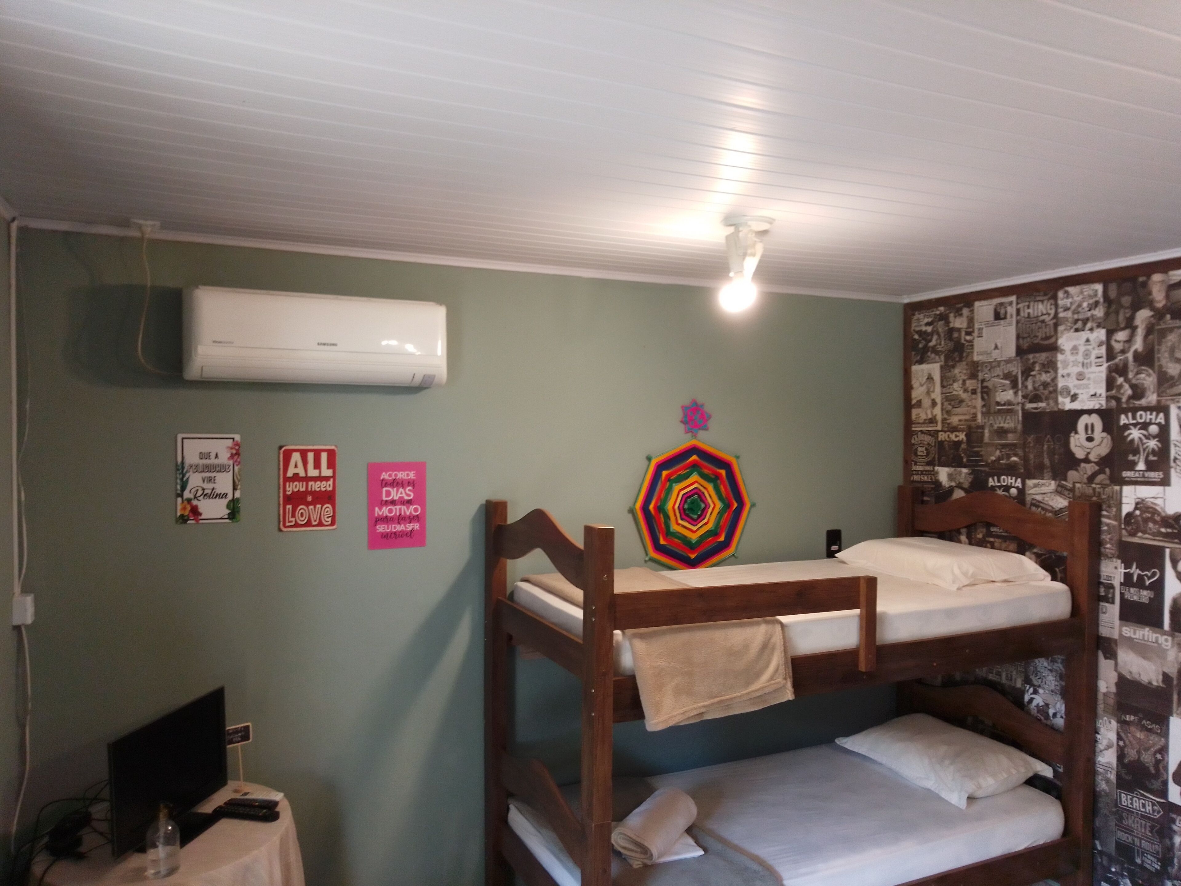 Une chambre avec un lit superposé, un ventilateur de plafond, un appareil de climatisation et un mur orné de divers affiches et panneaux.