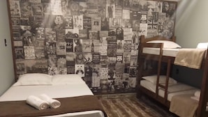 Une chambre avec un lit superposé, un lit simple et un mur recouvert de vieilles affiches.