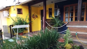 Un bâtiment jaune avec un porche en bois, des plantes en pot et une clôture en treillis métallique.