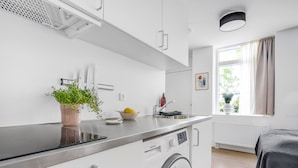 Cuina moderna amb rentadora integrada, una planta en test i una finestra amb cortines.