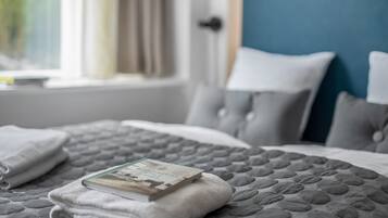 A neatly made bed with a quilted cover, a folded white towel, and a book on top.
