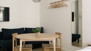 Habitació moderna amb una taula rodona de fusta, dues cadires, un penjallum, un mirall i un llit.