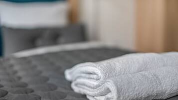 Une serviette blanche, soigneusement pliée, est posée sur un lit recouvert d’une couverture matelassée grise.
