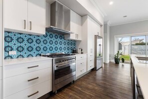 Une cuisine moderne avec des meubles blancs, un pare-feu décoratif, des appareils en acier inoxydable et une vue sur l’extérieur.